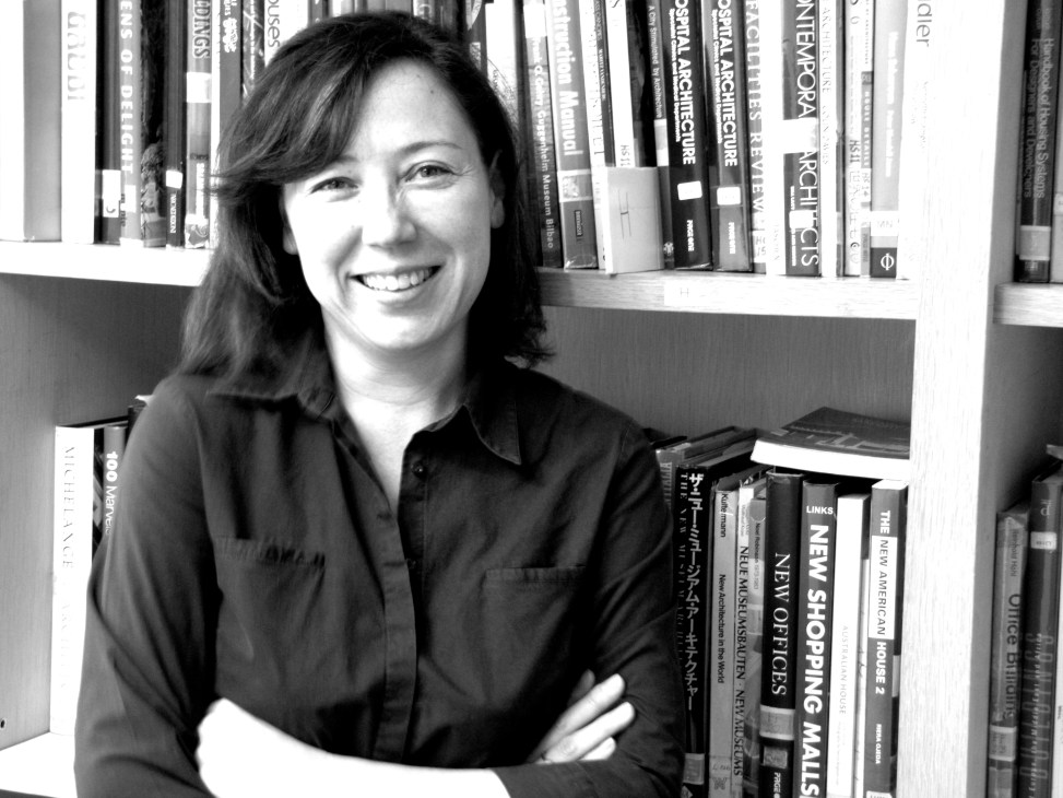 Architect Serina Hijjas smiling in front of a bookshelf filled with architecture and design books.
