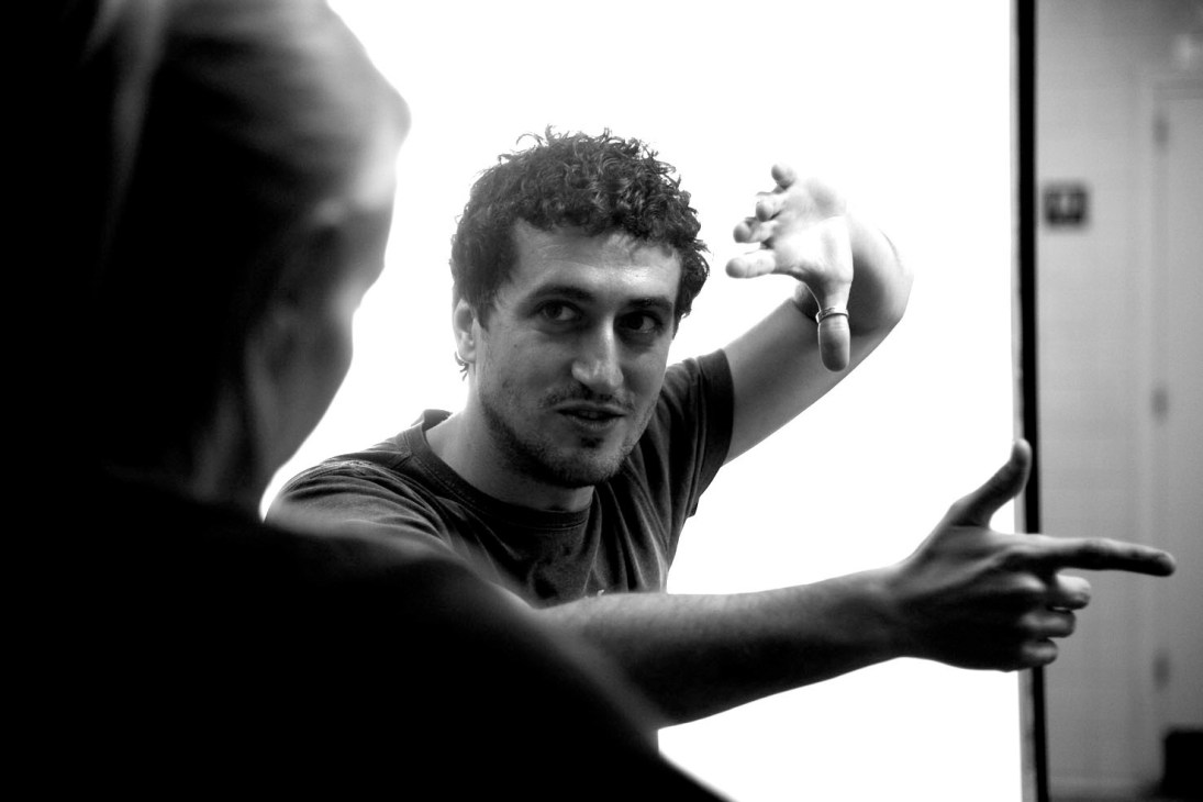 Black and white portrait of Spanish film director Guillem Morales in conversation with another person.