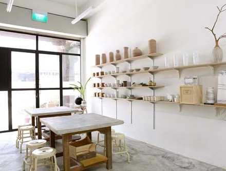 Minimalist retail space with wooden table, woven stools, and shelves displaying ceramic vessels and home goods.