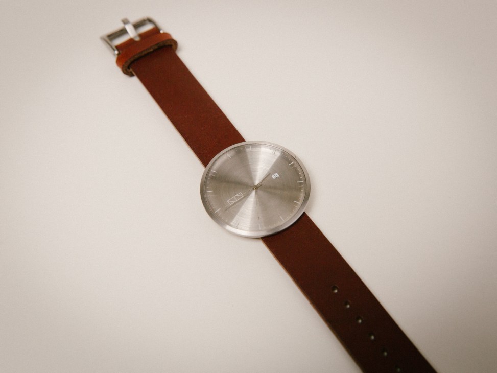 W1/D watch with brushed steel face and cognac leather strap on white background