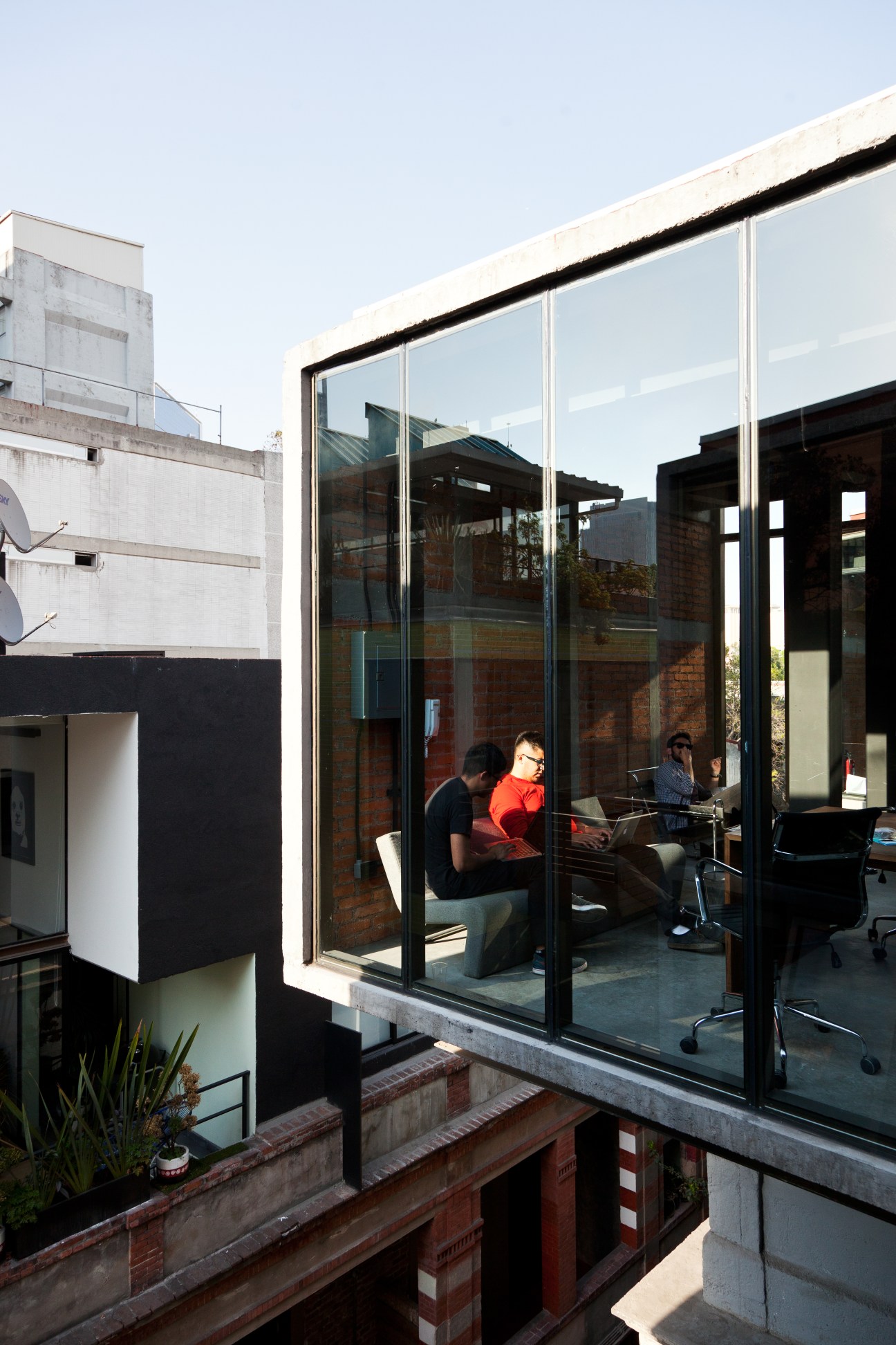 Modern glass-walled office with black frames overlooking historic brick buildings in Mexico City's Colonia Roma neighborhood.
