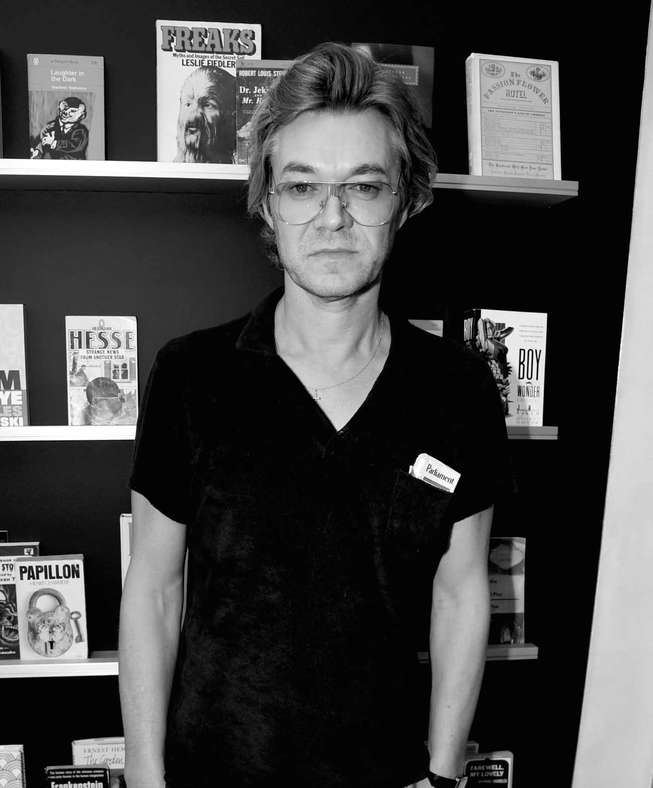 Man with glasses wearing black shirt standing in front of shelves displaying vintage movie posters and publications.