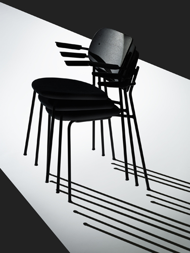 Stacked black chairs with metal legs casting shadows on a diagonal split background.