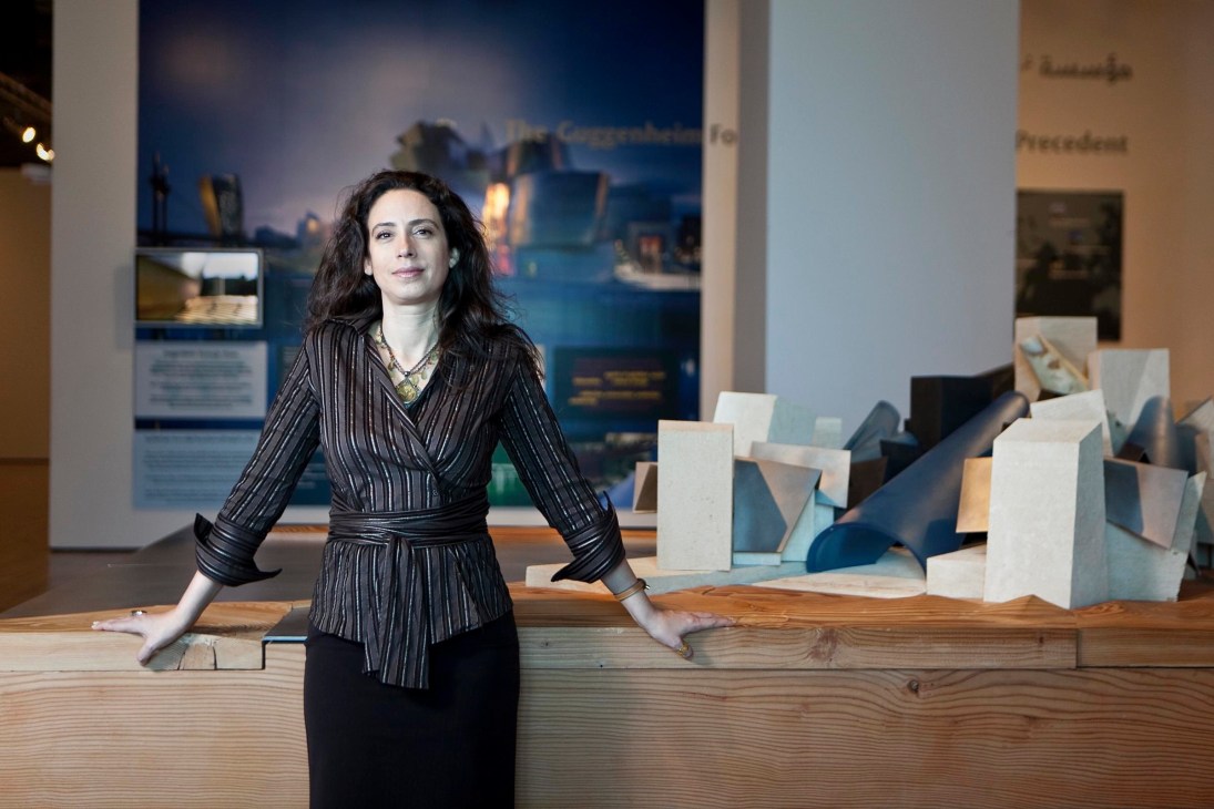 Rita Aoun-Abdo stands at a wooden desk with architectural models behind her in an exhibition space.