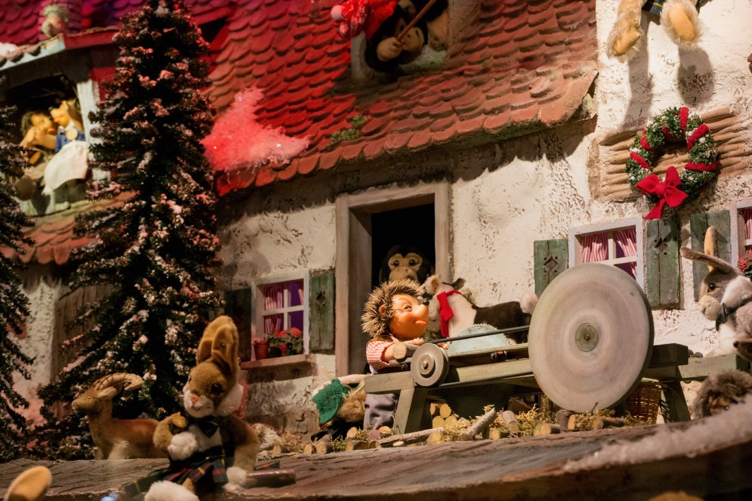 Vintage Christmas window display featuring toy animals and characters in a woodland cottage scene with red roof.