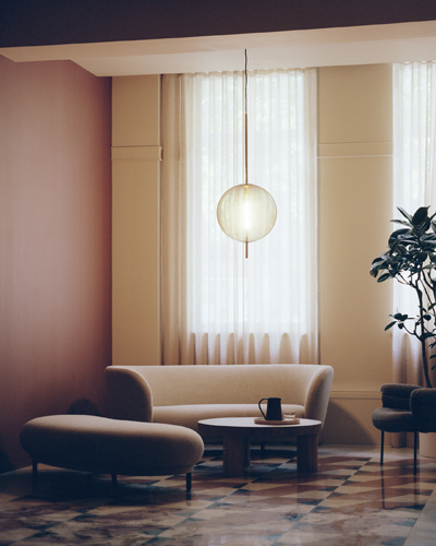 Modern office lobby with curved beige sofa, pendant light, potted plant, and floor-to-ceiling windows with sheer curtains.