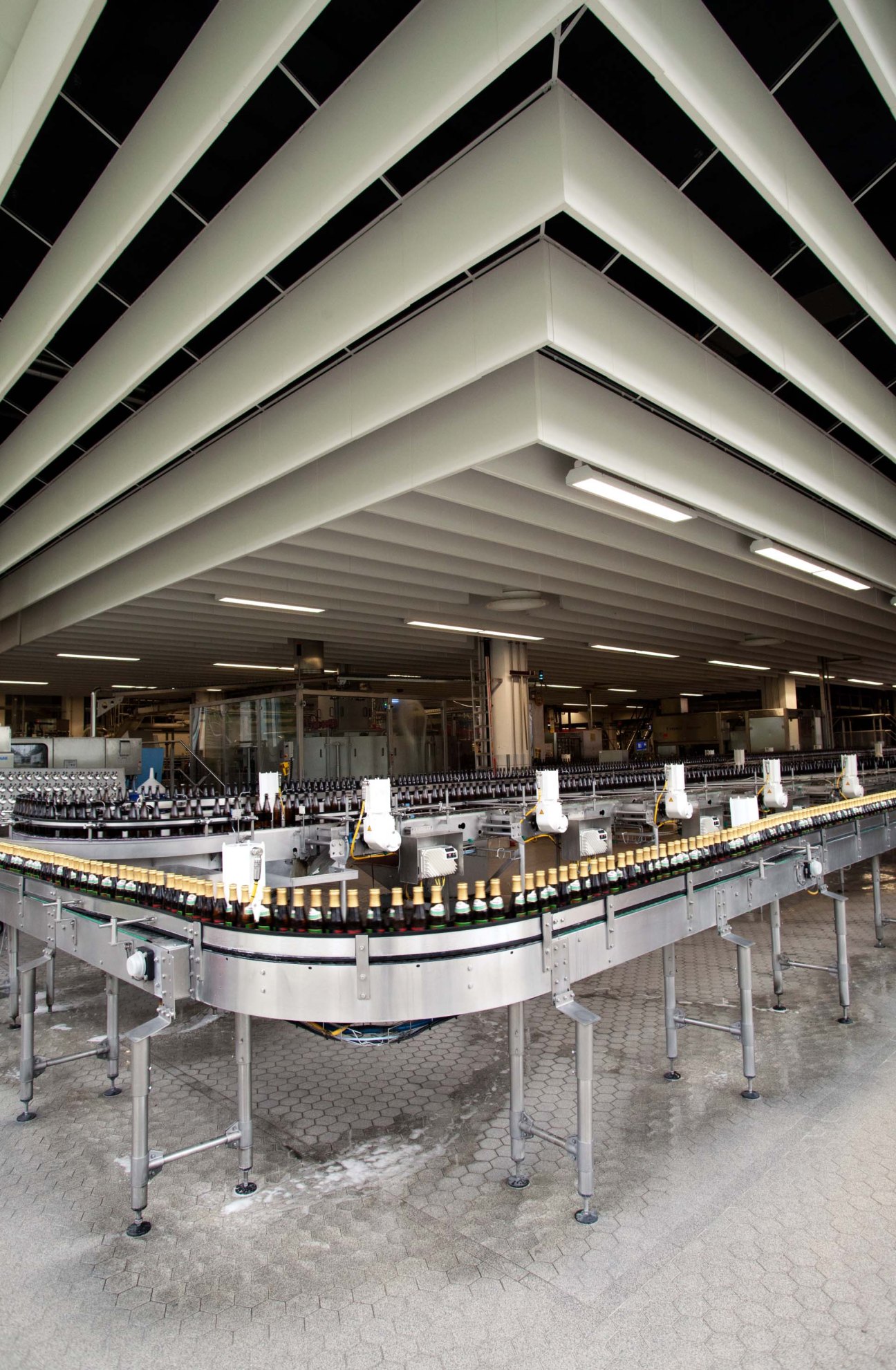 Modern brewery bottling line with conveyor system and automated machinery filling beer bottles under industrial ceiling lights.