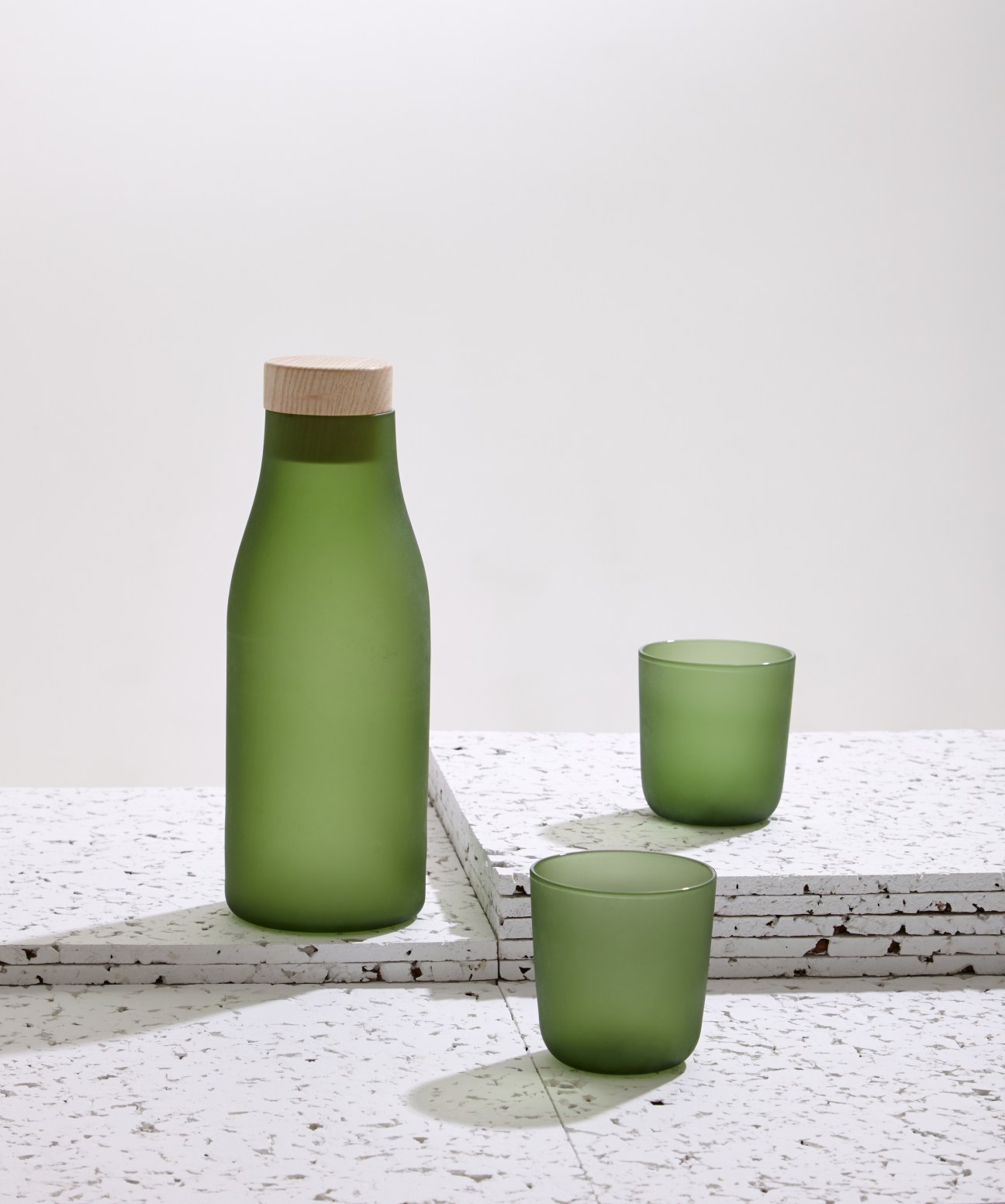 Green glassware set with a carafe and two cups on a speckled surface