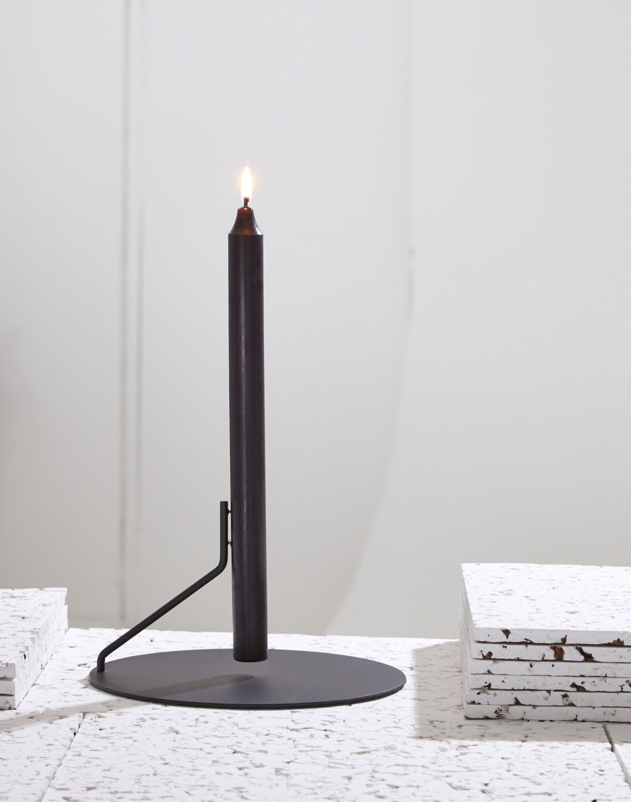 Buka candlestick by Diis with a lit black candle on a circular base.