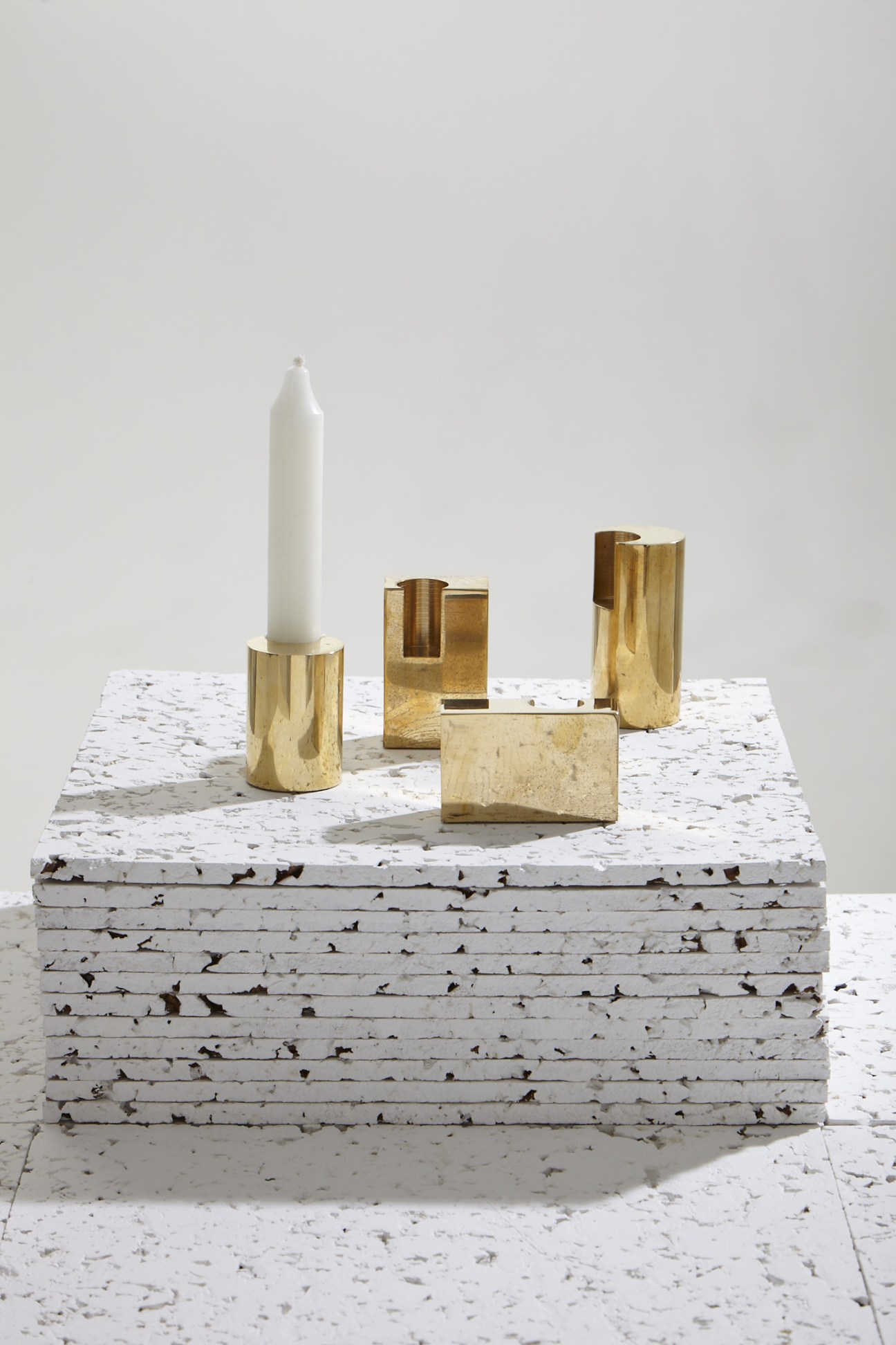 Lump brass candlesticks by Kim Thome displayed on a white textured surface with a lit candle.