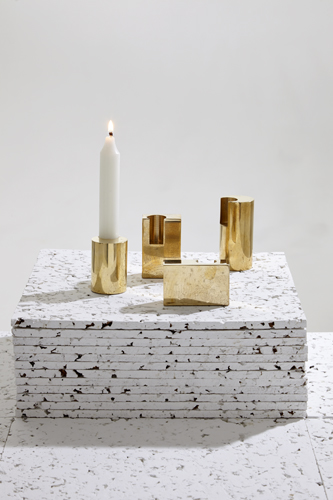 Brass candlesticks with a white candle arranged on a textured white surface.