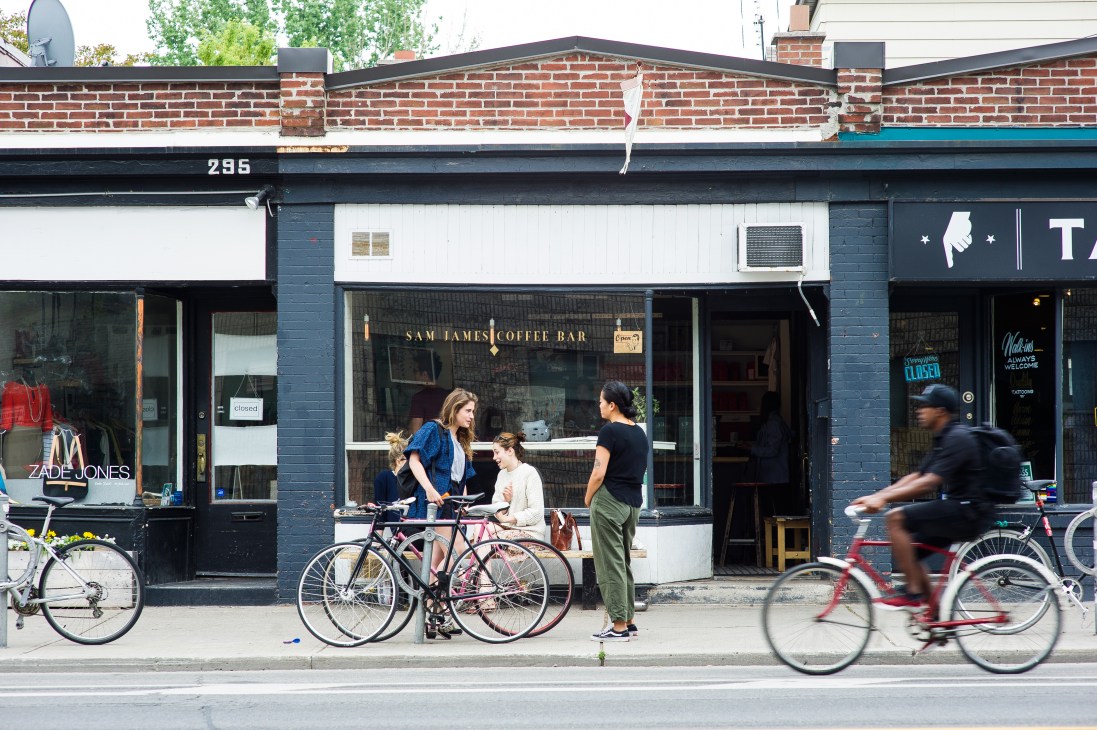Sam James Coffee Bar storefront on a Toronto street with customers and cyclists outside.