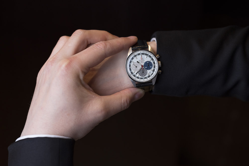 Hand holding Zenith El Primero watch with gold casing and white dial against black background
