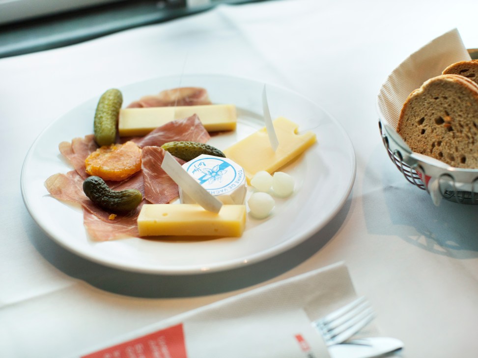 SBB Plättli charcuterie platter with Swiss ham, cheese, pickles, pearl onions and bread on white plate.