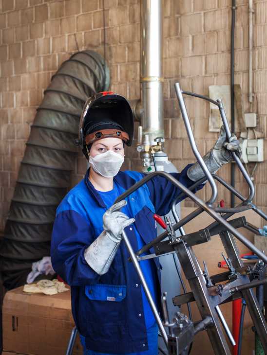 Worker in blue uniform welding metal chair frame in factory workshop.