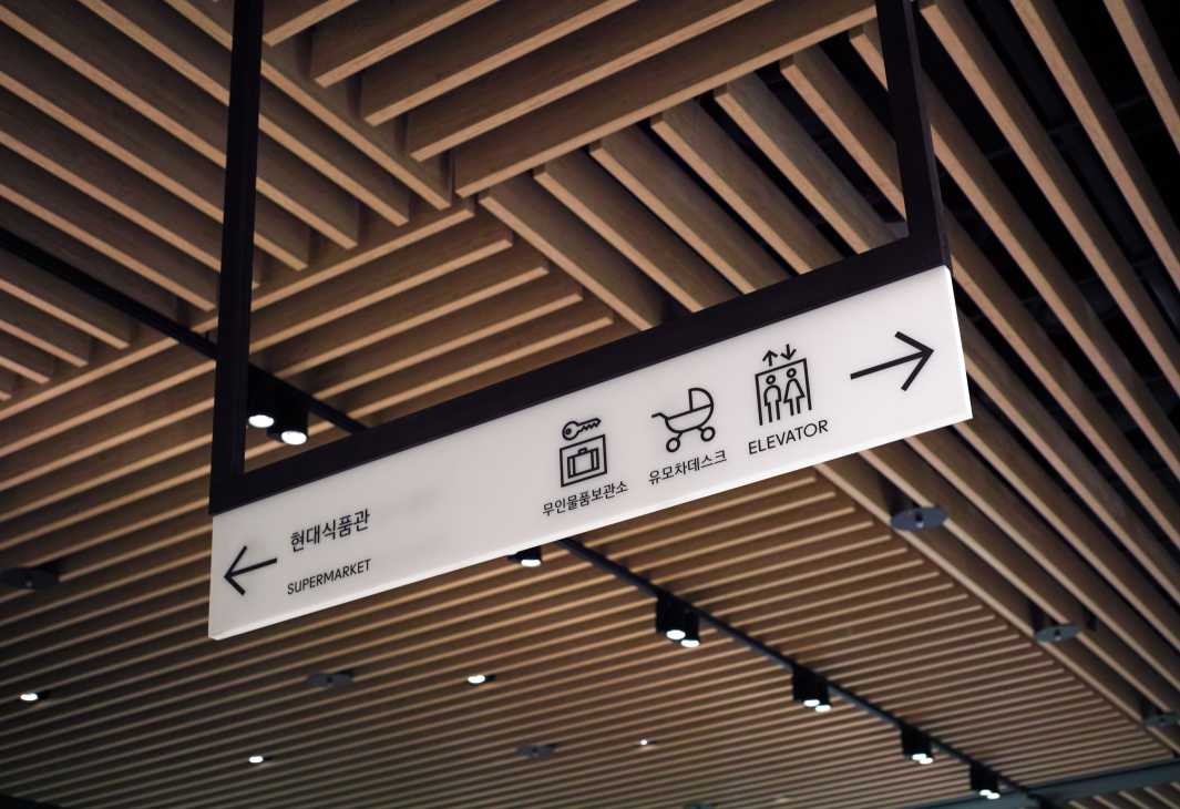Hyundai Department Store wayfinding signage with sans serif fonts and icons on white background against wooden ceiling.