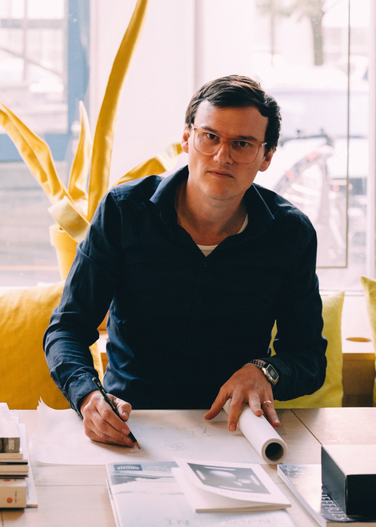 Chris Middleton sits at a desk with papers and pen, yellow sculptural elements visible behind him