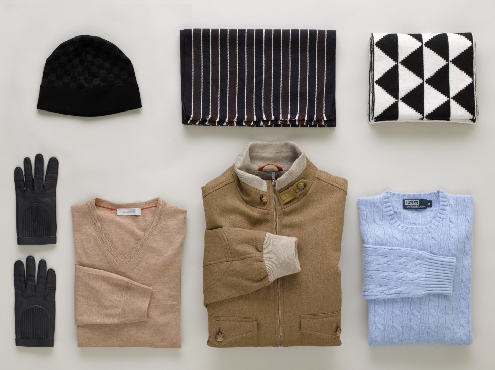Styled flat lay of après-ski apparel including hats, scarves, gloves, jumpers and a jacket in neutral tones.