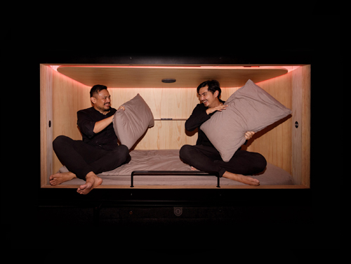 Two founders sit facing each other inside a minimalist sleep pod with wooden walls and warm lighting.