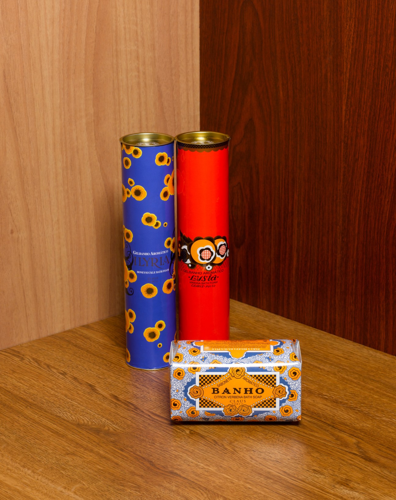 Two decorative cylindrical containers and a boxed soap product displayed on a wooden surface against a wooden backdrop.