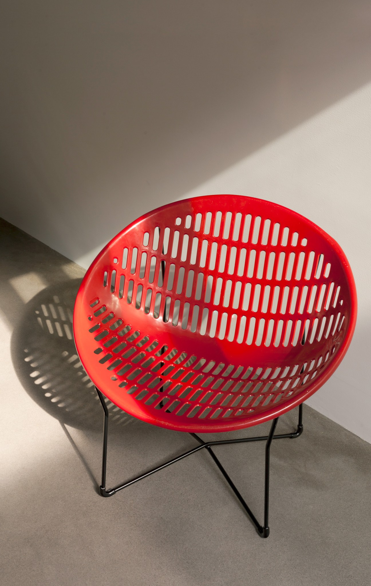 Red Solair Chair with perforated plastic seat and black steel frame in corner setting with dramatic shadows