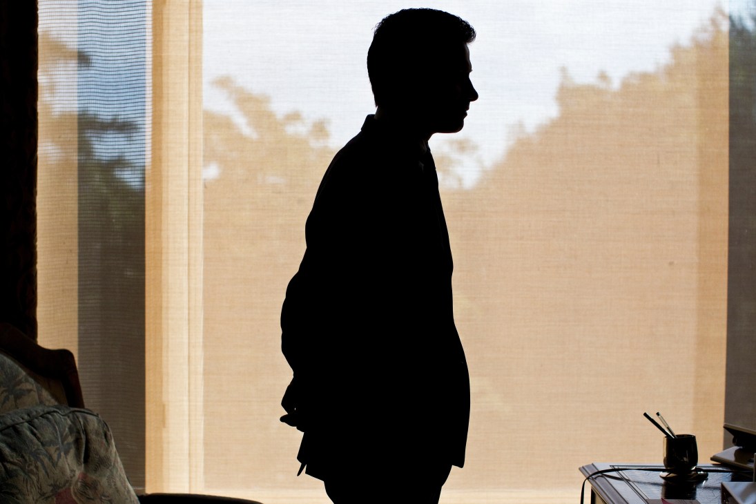 Silhouetted man in business attire standing by a window overlooking a desert landscape.