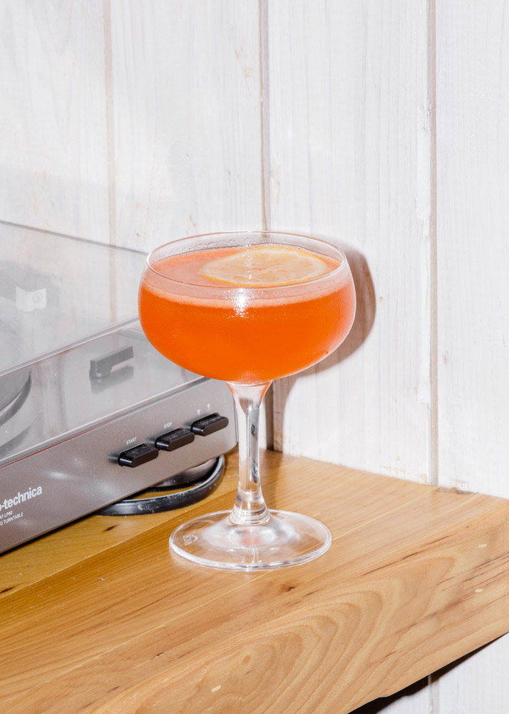 Orange cocktail in a coupe glass on a wooden surface.