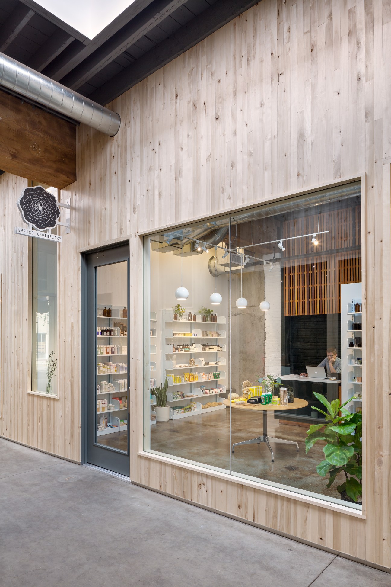 Spruce Apothecary storefront in Portland with light wood facade, large windows displaying beauty products and interior shelving.