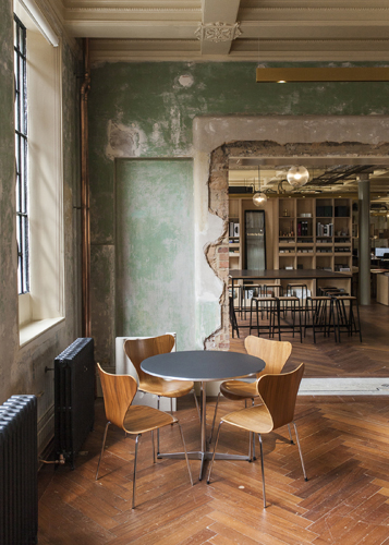 Minimalist workspace with round table, wooden chairs, and exposed green wall in converted factory.