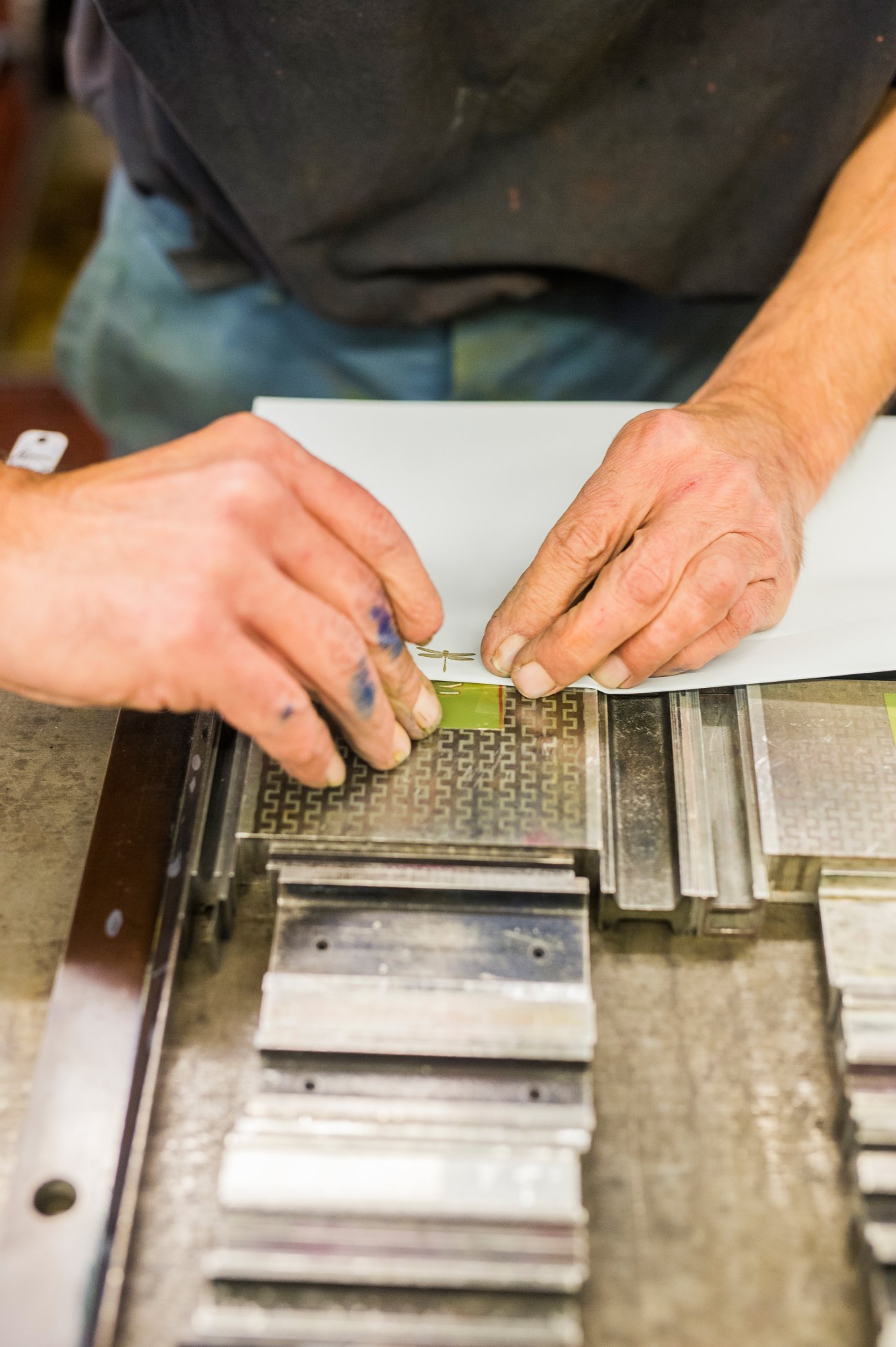 Hands aligning lead letter blocks with tweezers in a printing press for typesetting.