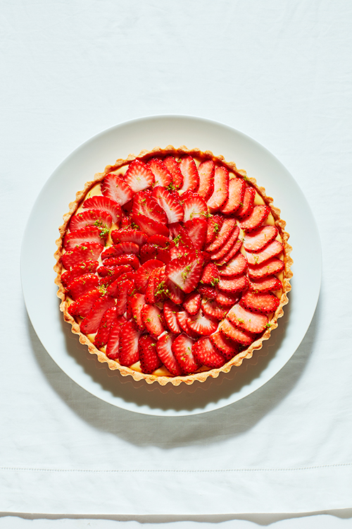 A strawberry tart with sliced red strawberries arranged in a spiral pattern on a custard filling in a pastry shell, served on a white plate.