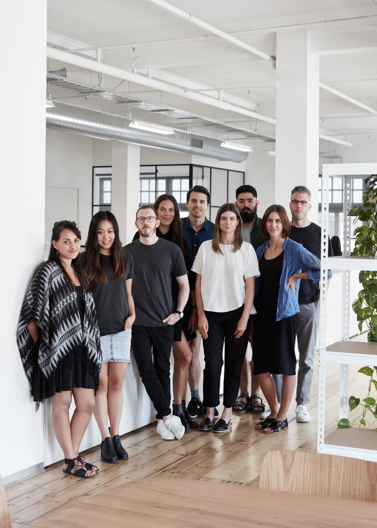 Team of designers standing together in a bright, open studio space with industrial ceilings and plants.
