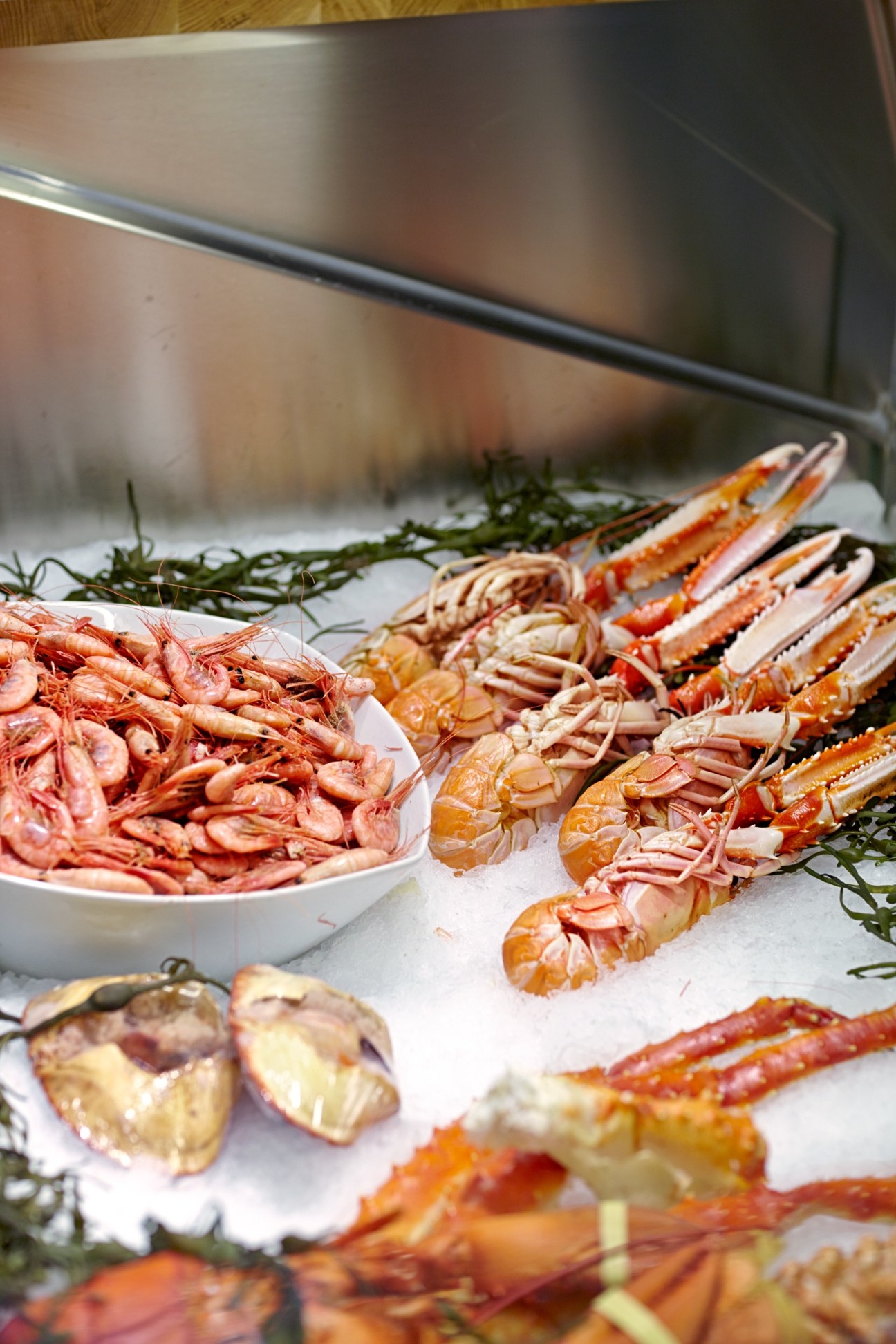 Shellfish display with shrimp, langoustines, scallops and seaweed garnish on ice.