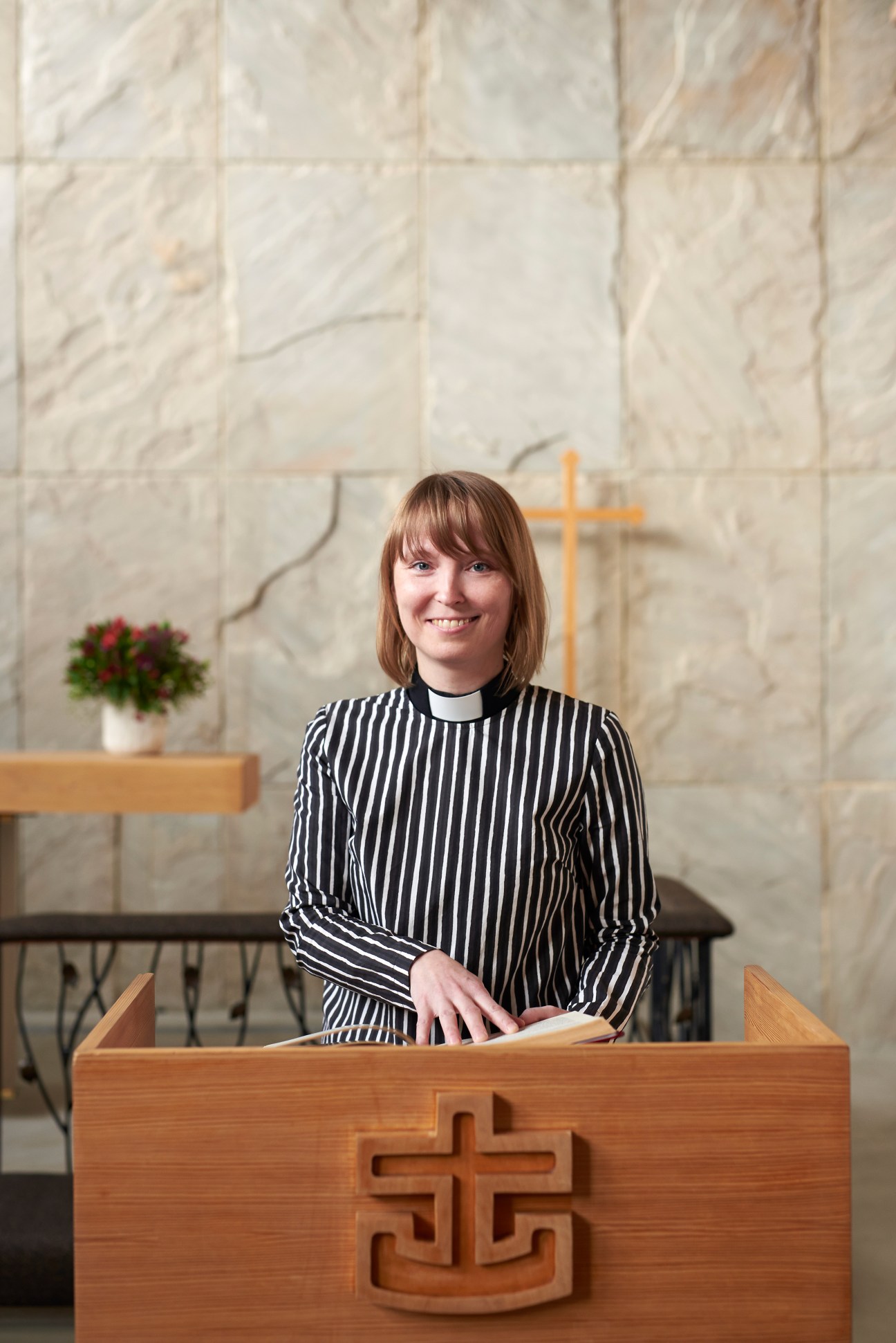 Woman in striped shirt standing at wooden altar with cross in modern church interior.