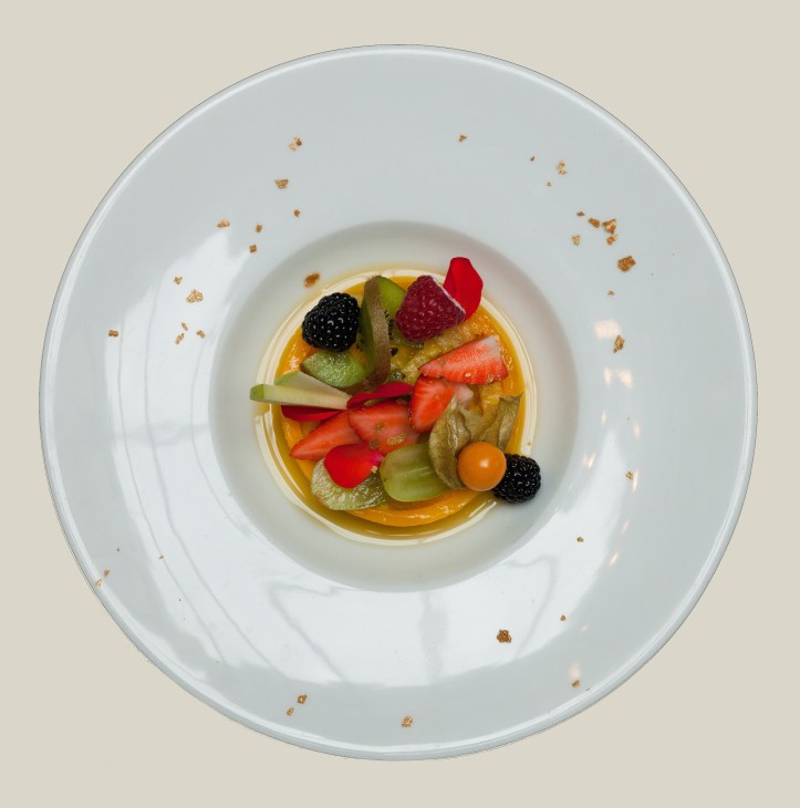 Elegant plated fruit salad with berries, kiwi, and other fresh fruits on white plate with scattered crumbs.
