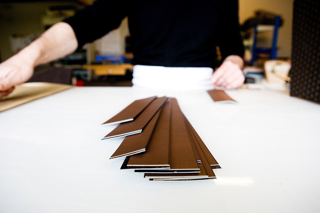 Artisan hands working with layered brown leather strips on a white surface in a workshop.