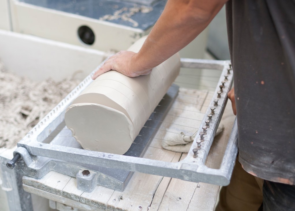 A craftsperson's hand positioning a white porcelain cylinder in a production mold during manufacturing.
