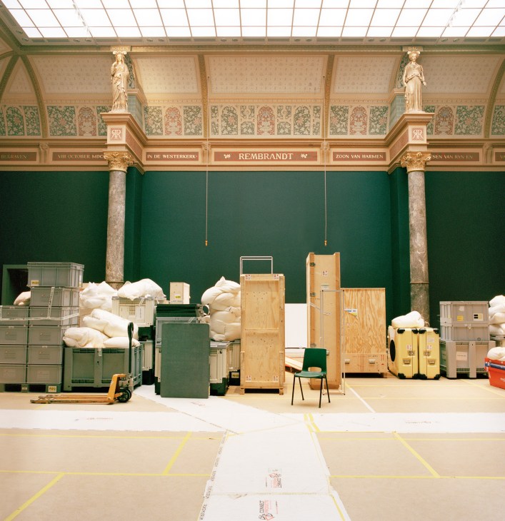 Interior of Rijksmuseum with ornate ceiling and green walls displaying museum collection boxes and wooden crates during relocation preparations.