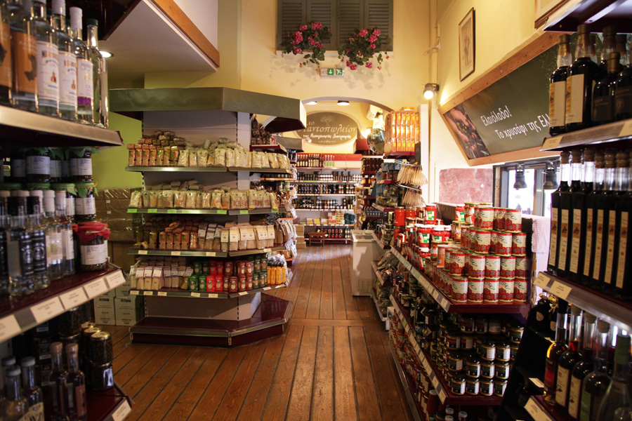 Interior of To Pantopoleion grocery store in Athens showing shelves stocked with products, flowers hanging above, and wooden flooring.