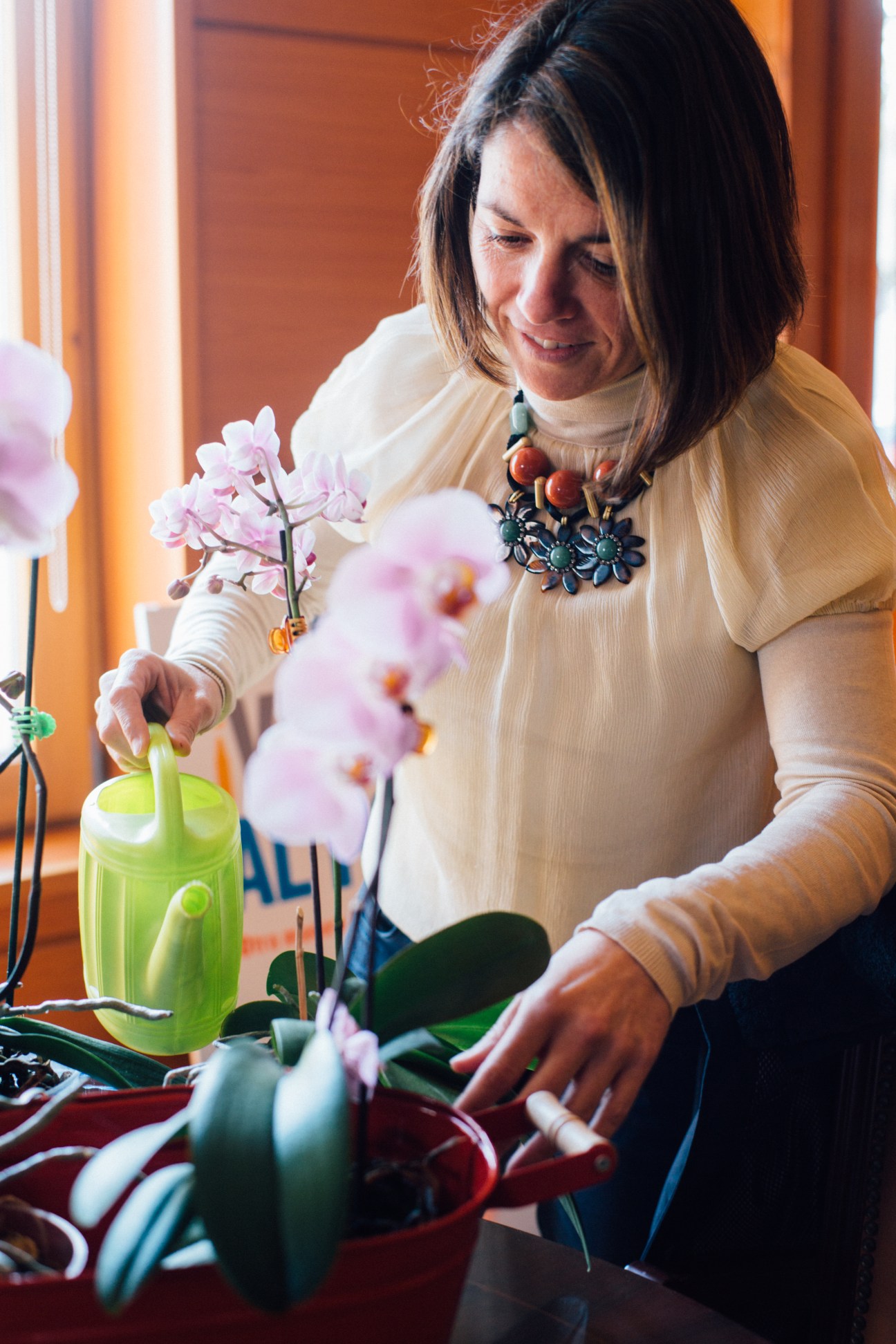 Woman arranging pink orchid flowers in a bright green watering can indoors.