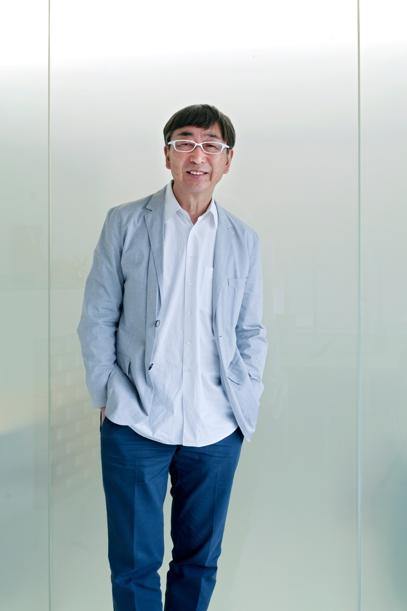 Architect Toyo Ito smiling at the camera, wearing glasses, a light blue blazer and white shirt.