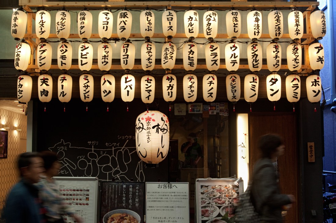 Japanese paper lanterns with handwritten calligraphy hanging above a restaurant storefront in Kyoto.
