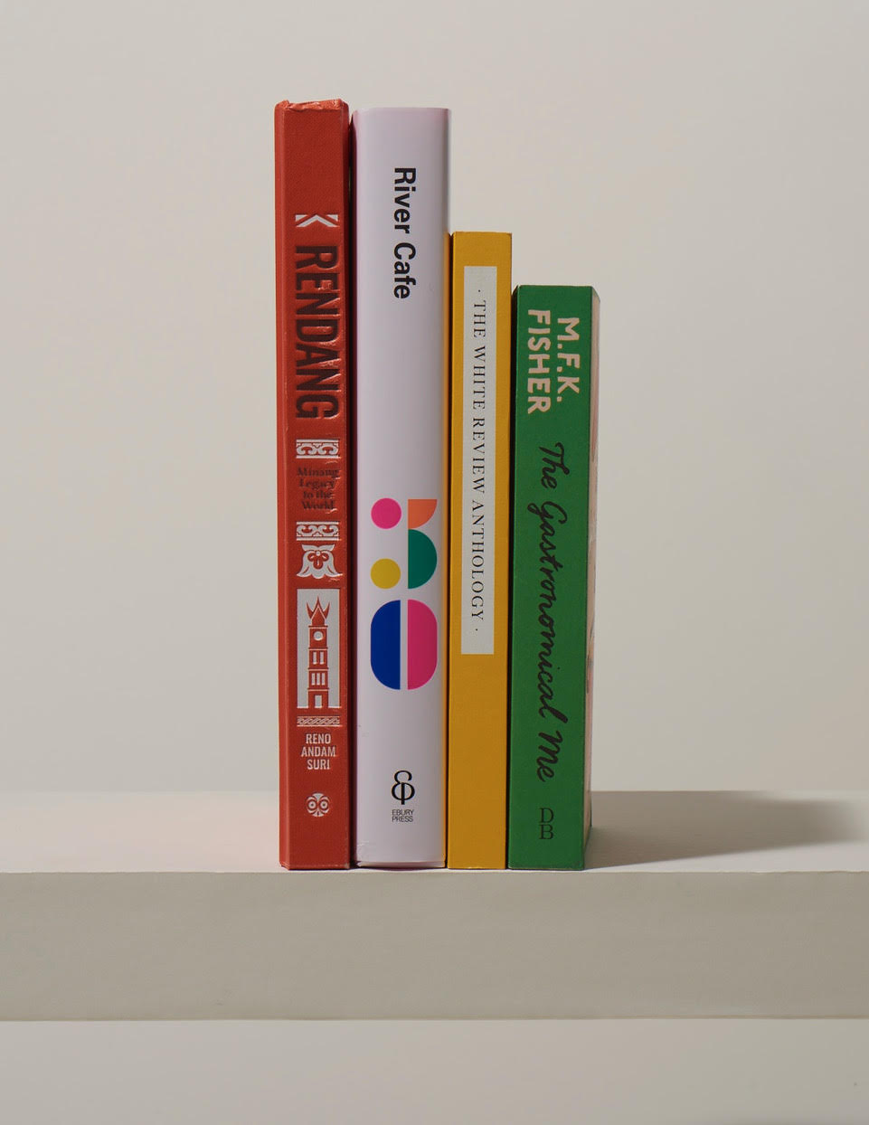 Four colorful book spines arranged vertically including Rendang, River Cafe, MFK Fisher, and other titles.