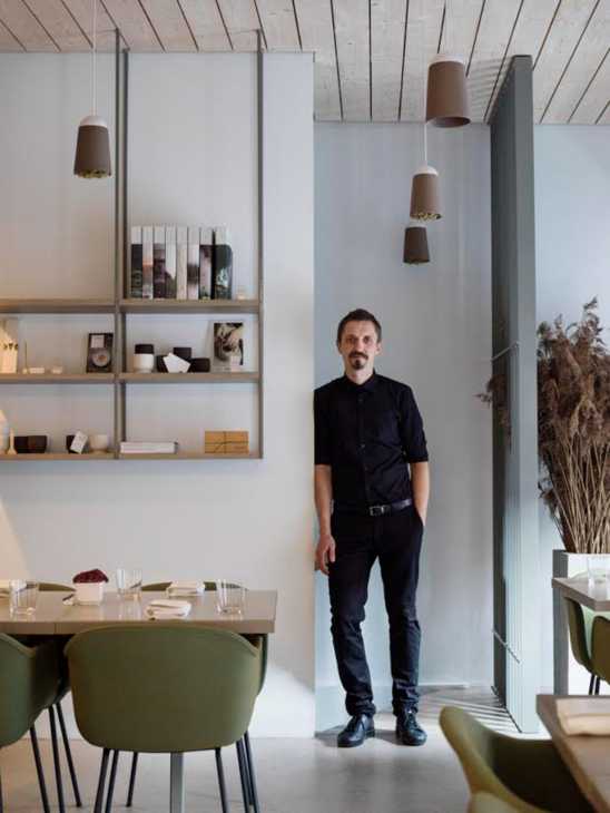 Man in black shirt standing in modern restaurant interior with pendant lights and shelving.