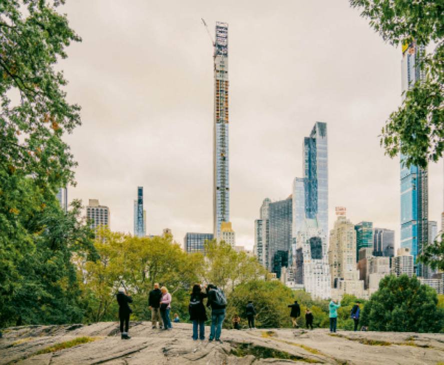 Manhattan skyline viewed from Central Park with tall modern skyscrapers framed by green foliage.