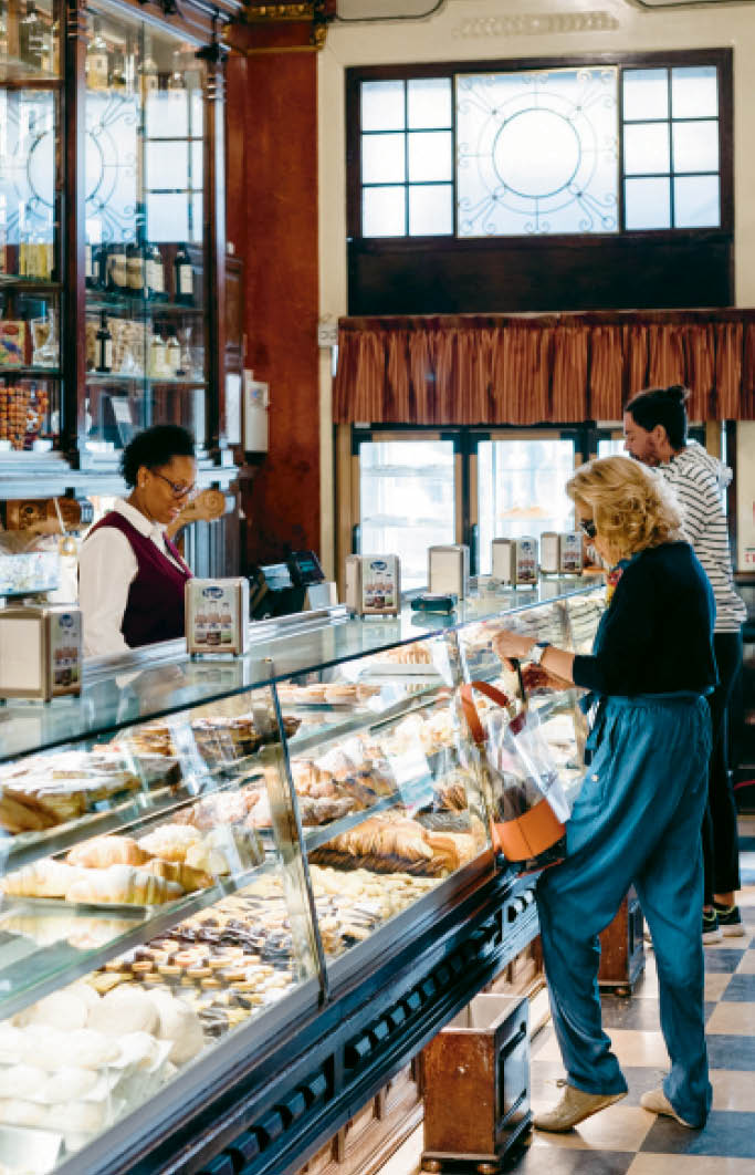Interior of Versailles Tearoom in Lisbon, a historic café with display cases of pastries and customers at the counter.