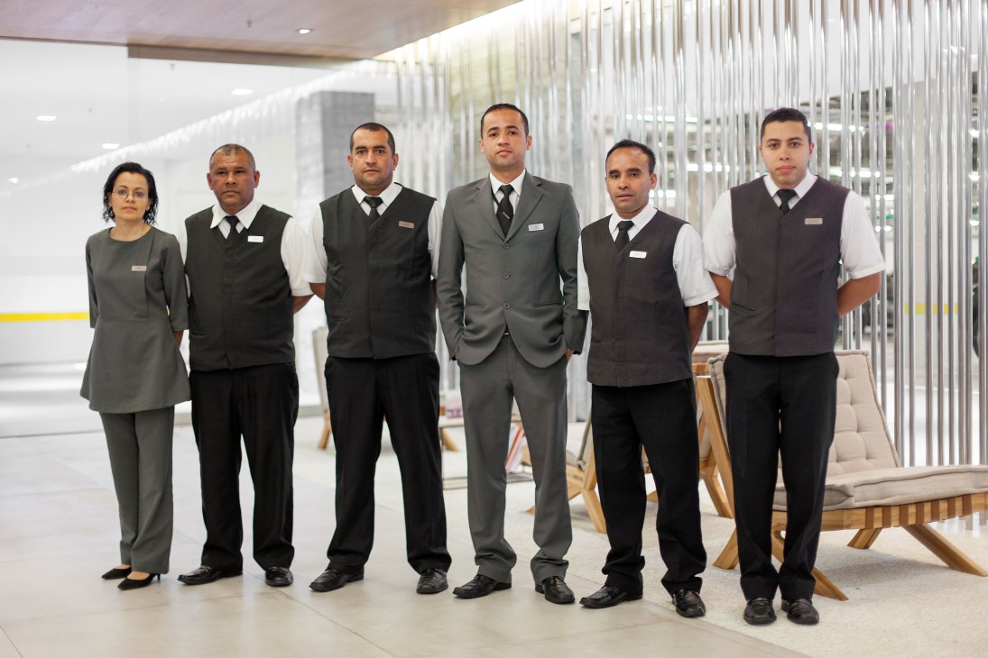 Six smartly dressed valet parking attendants stand in a modern luxury shopping center lobby.