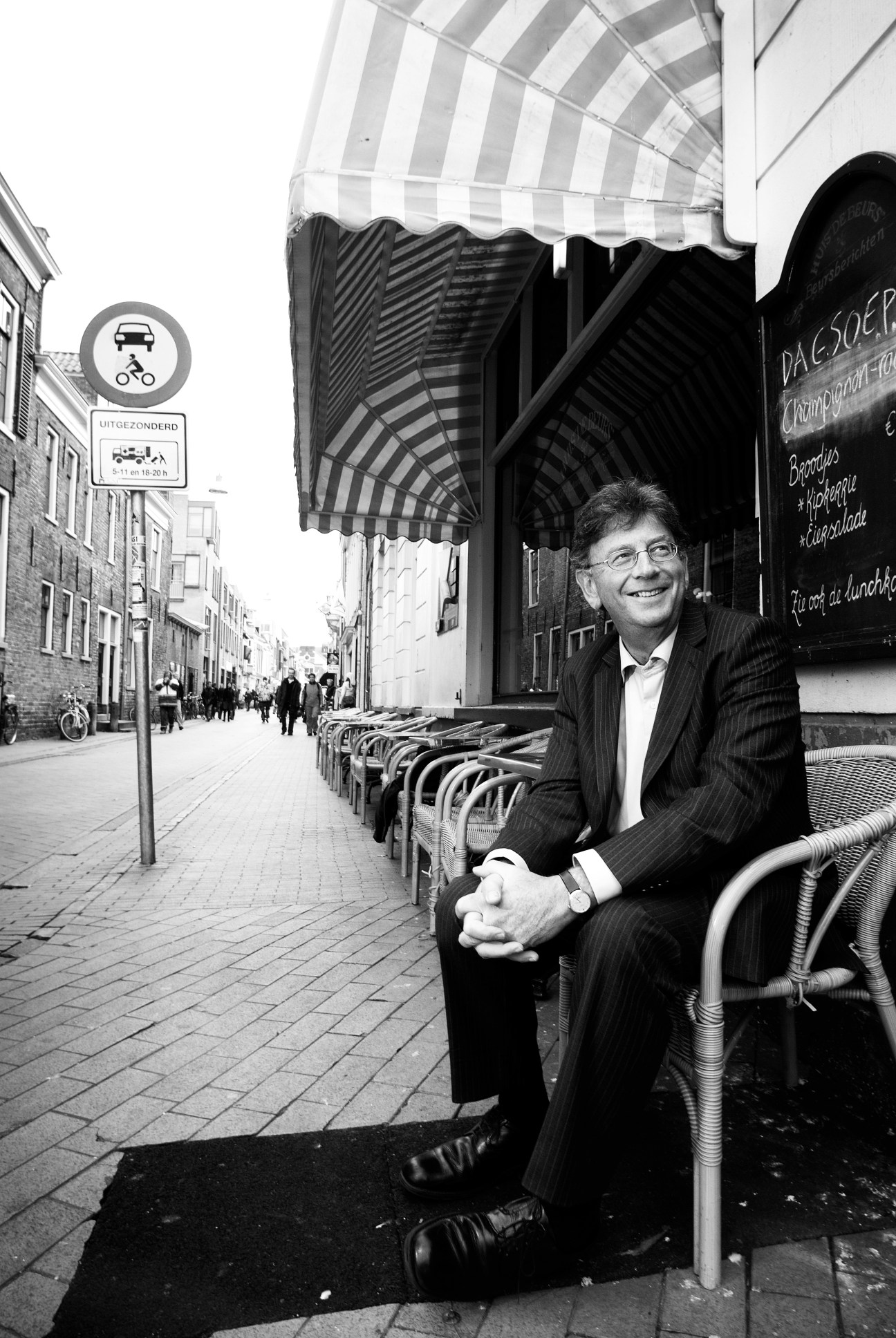 Jacques Wallage, Mayor of Groningen, seated outdoors on a European street with striped awning and bicycles visible.