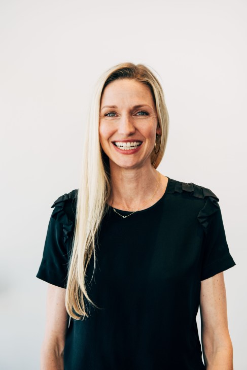 Woman with long blonde hair smiling at camera wearing black short-sleeved top