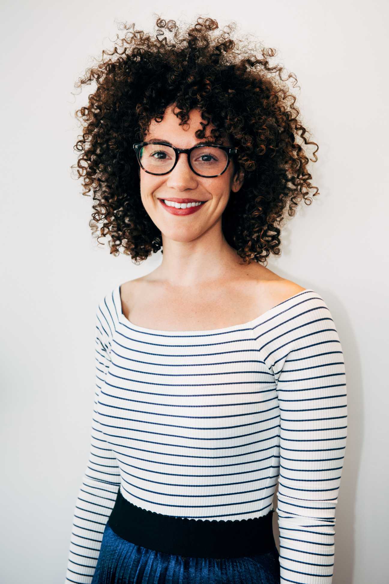 Portrait of a woman with curly brown hair and glasses wearing a striped blue and white top.